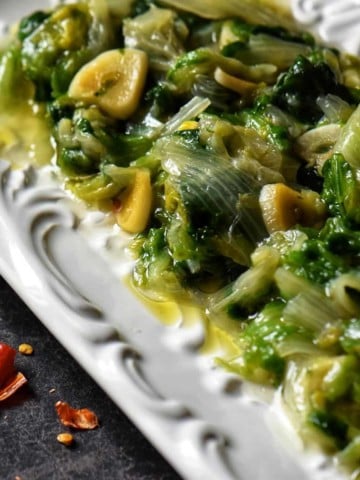 Sauteed Escarole with lots of garlic and red pepper flakes on a white platter.