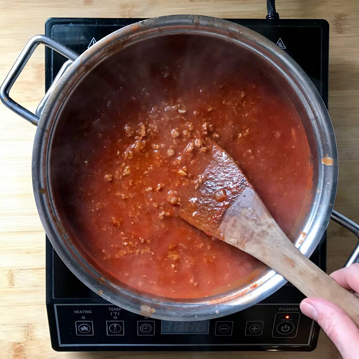 Cooked ground meat added to a simmering tomato sauce.