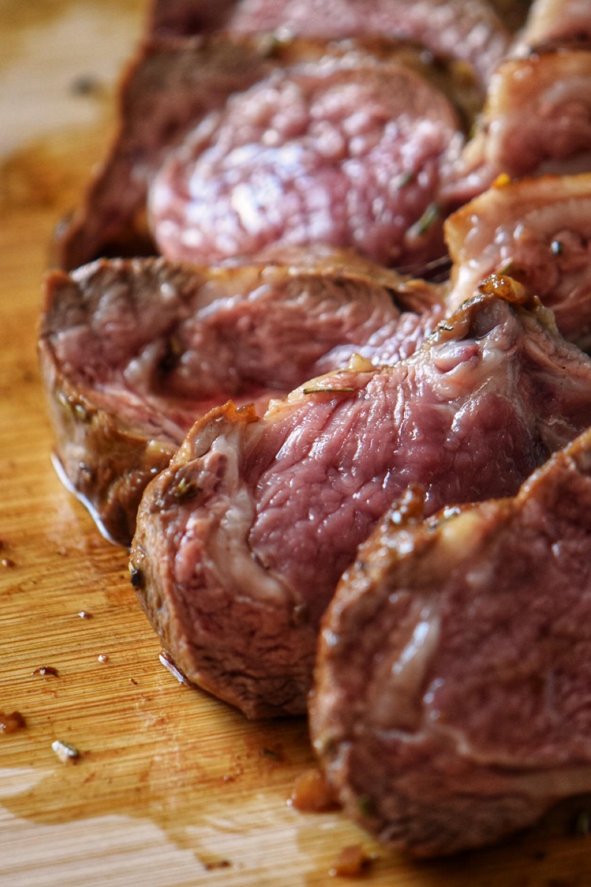 A close up shot shows the pinkness of pan seared lamb chops on a wooden board.