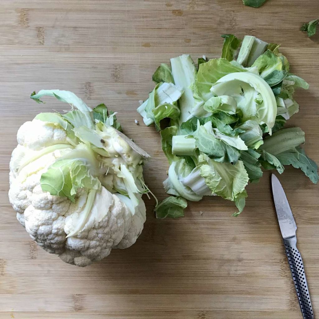 A head of cauliflower on a wooden board with the outer large leaves removed.