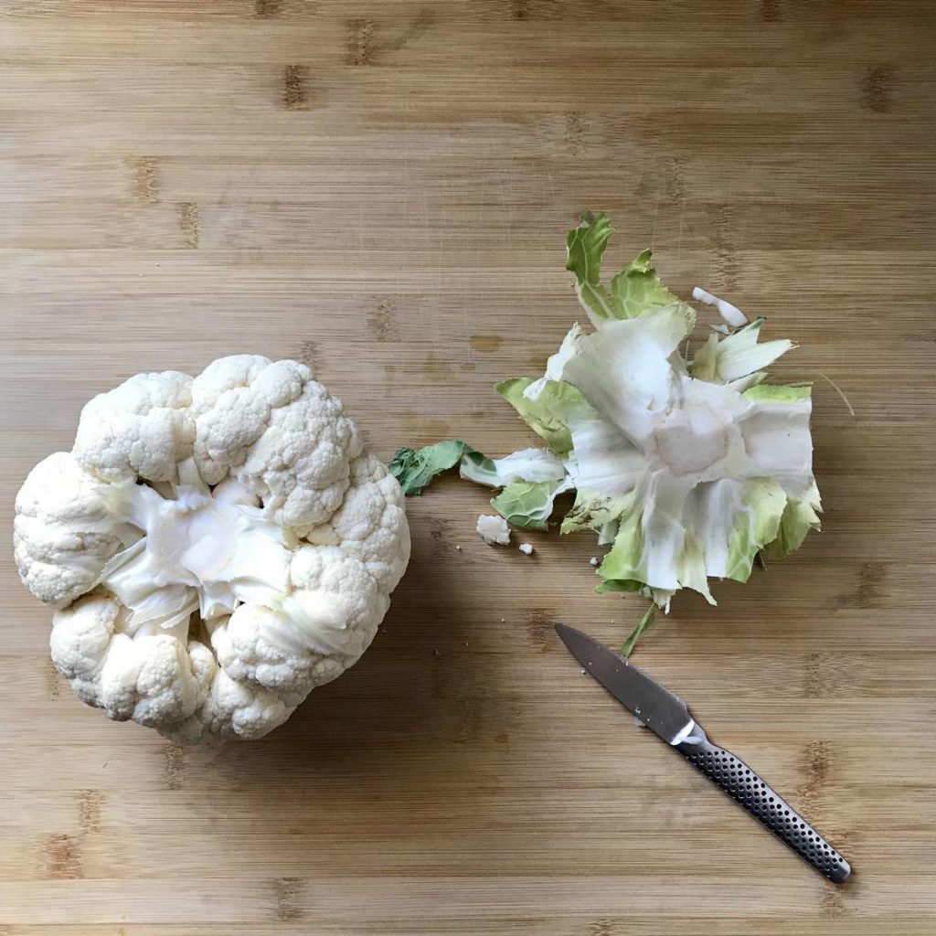 A cauliflower on a wooden board with the stem removed.