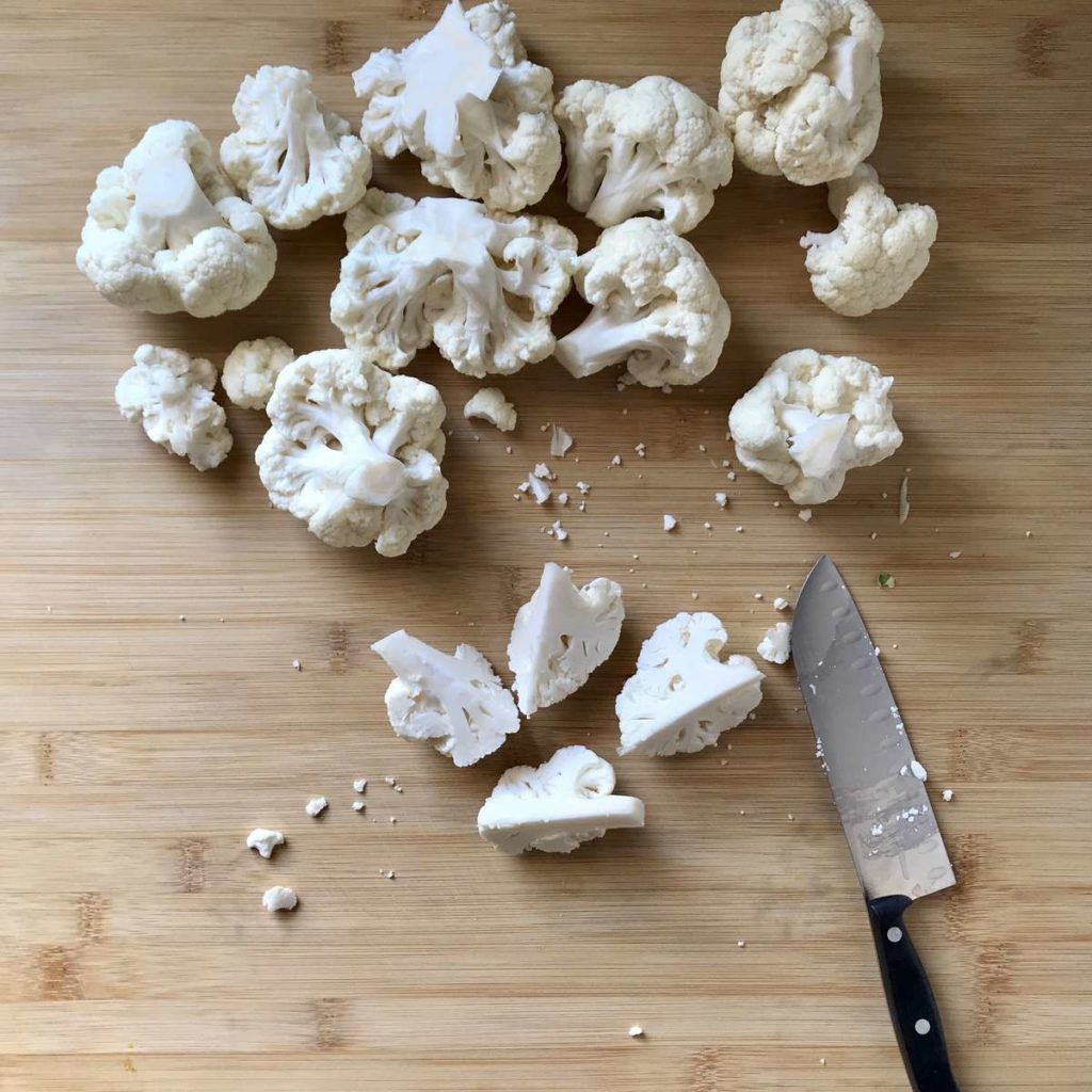 Sliced cauliflower florets on a wooden board.