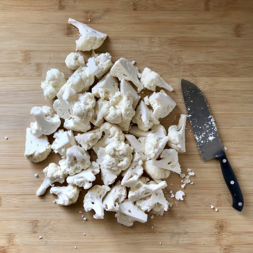 Sliced cauliflower florets on a wooden board.