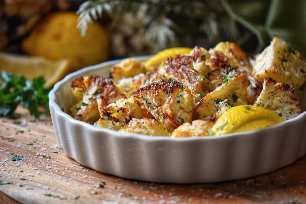 Cheesy roasted cauliflower in a white ceramic serving dish.