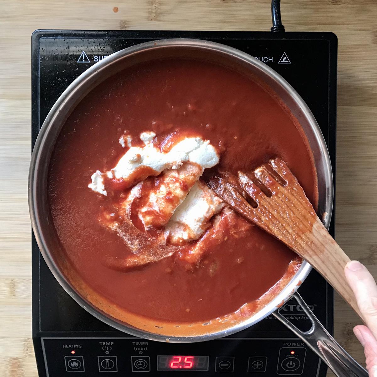 Ricotta cheese is added to tomato sauce in a saucepan.