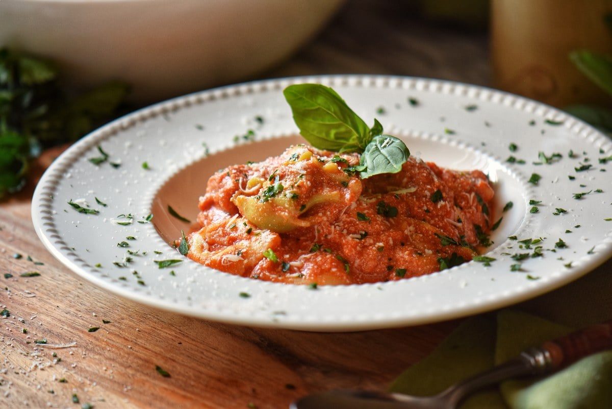 Tortellini in a white dish garnished with Italian parsley and basil.