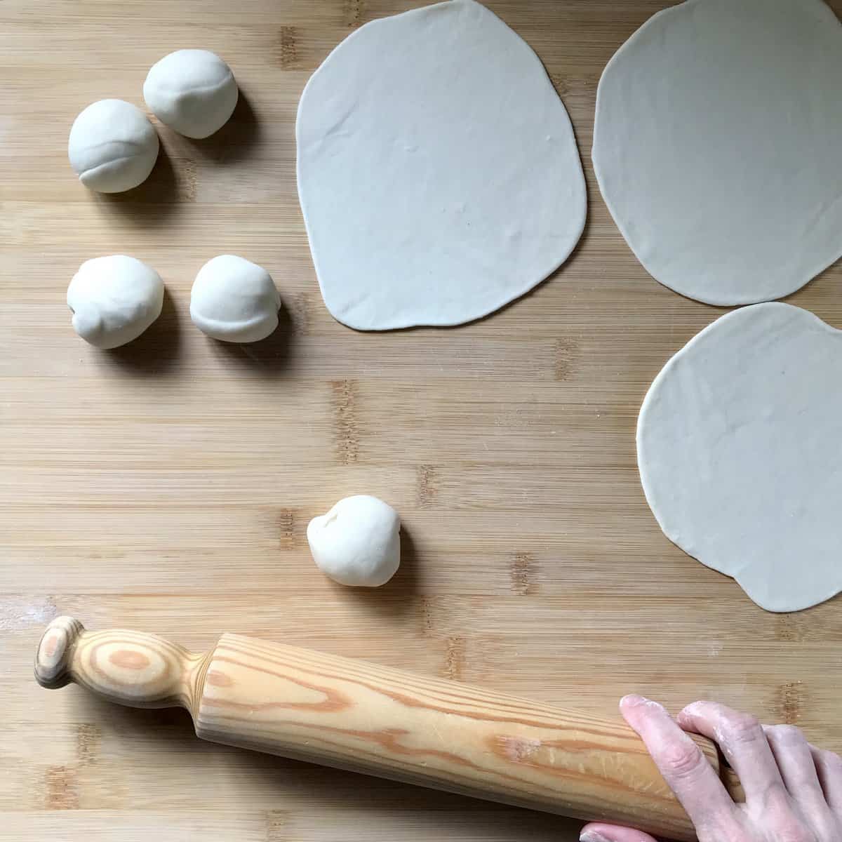 A rolling pin next to balls of dough on a wooden board.