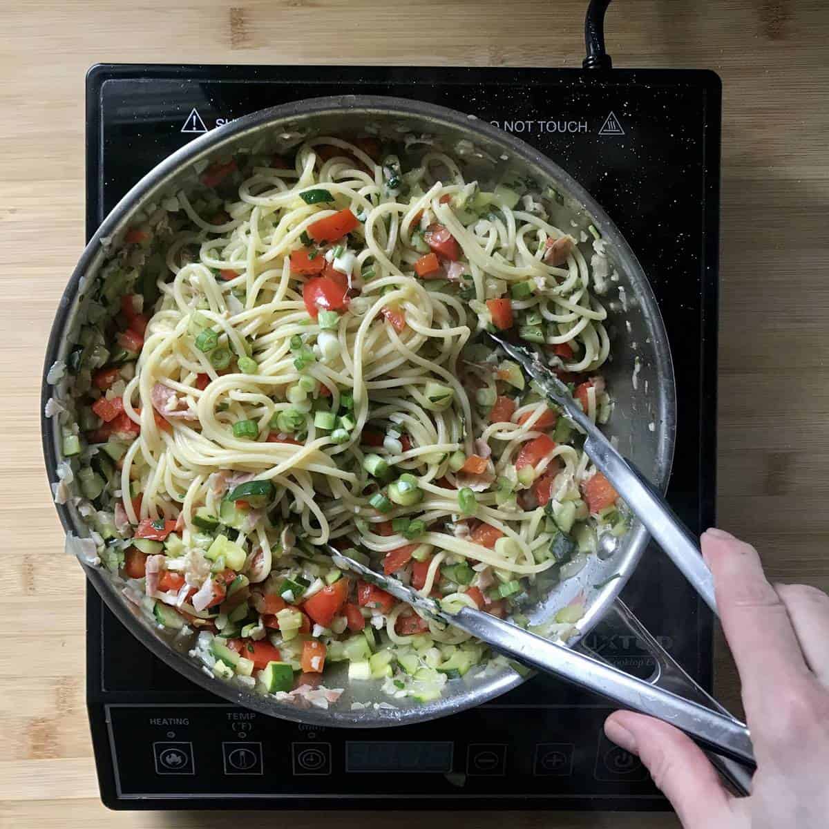 A spaghetti pasta recipe in a pan with sauteed vegetables.
