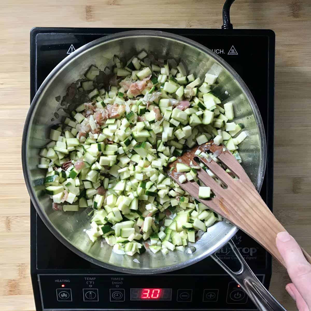 Diced zucchini in the process of being sauteed in a large pan.