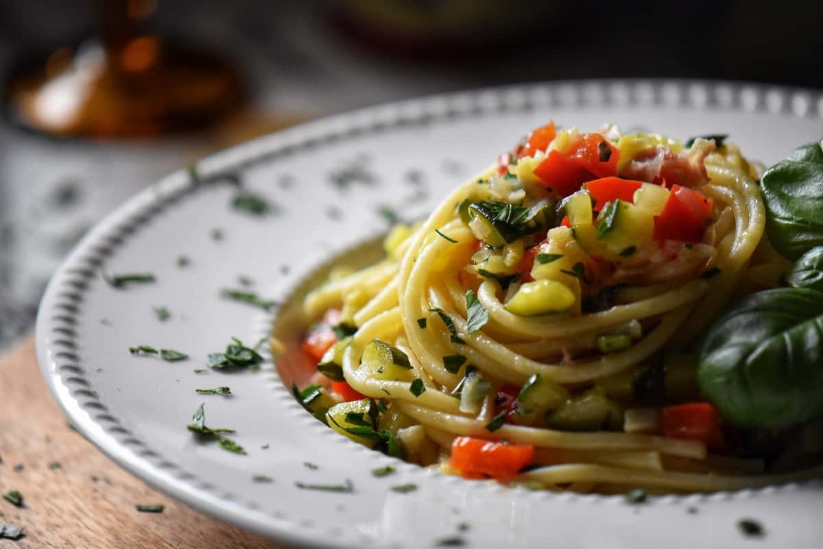 Spaghetti topped with sauteed vegetables in a white plate.