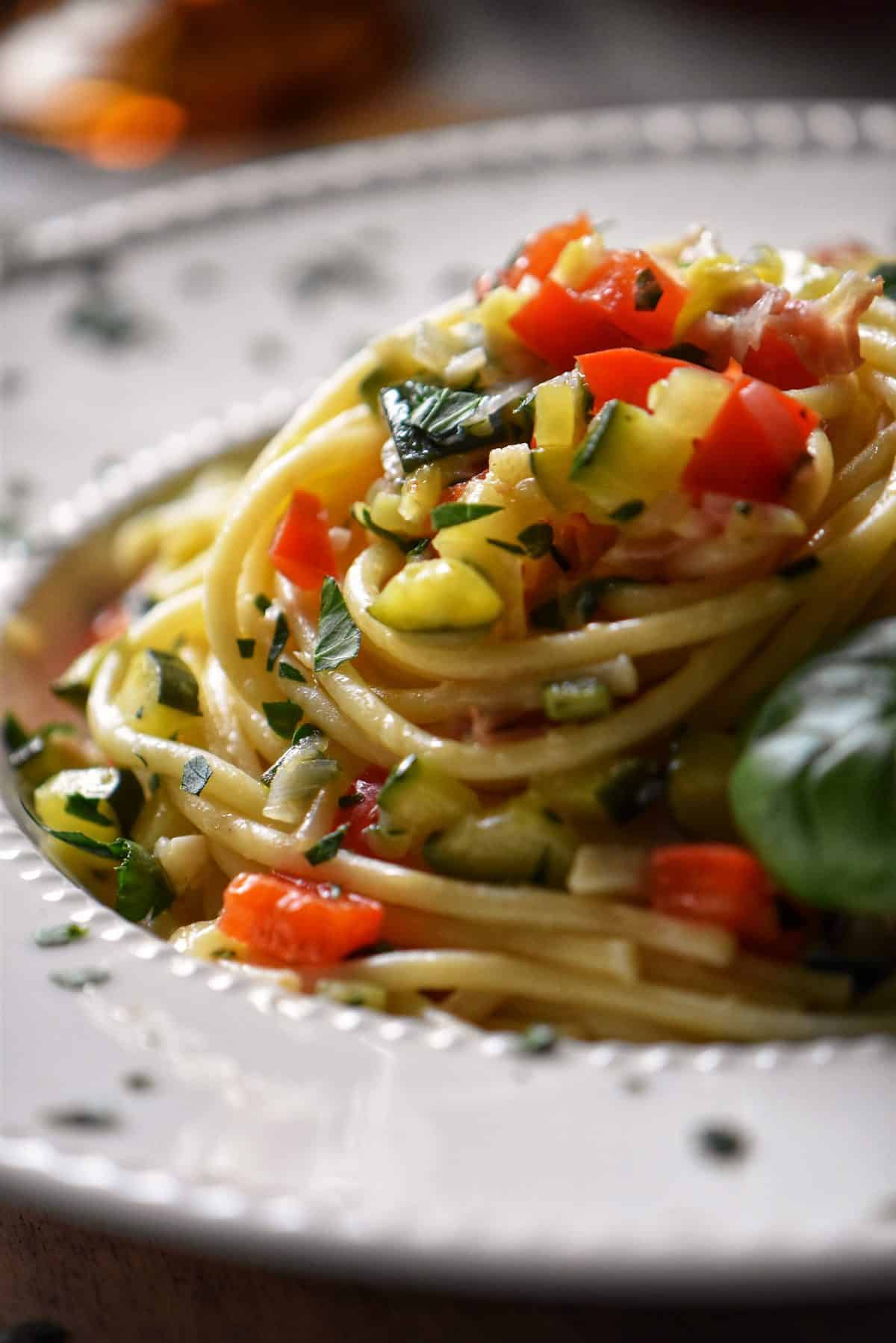 A plate of spaghetti topped with red peppers and zucchini.