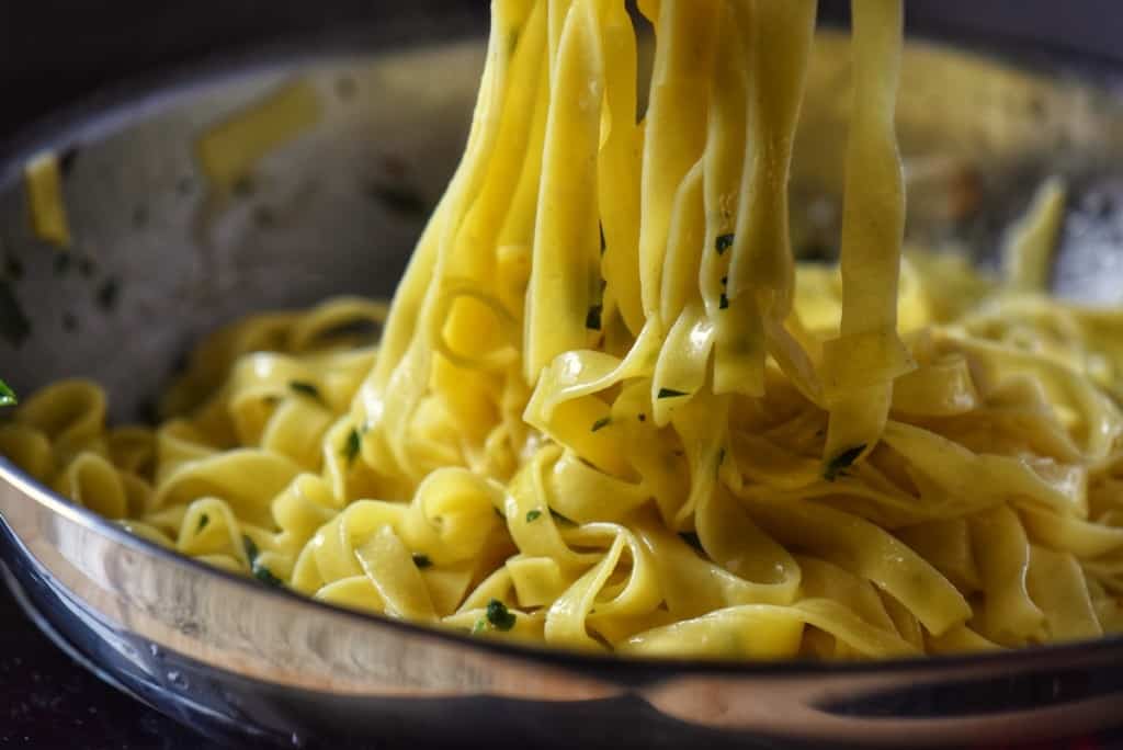 Pasta being combined with parsley and grated cheese in a pan.