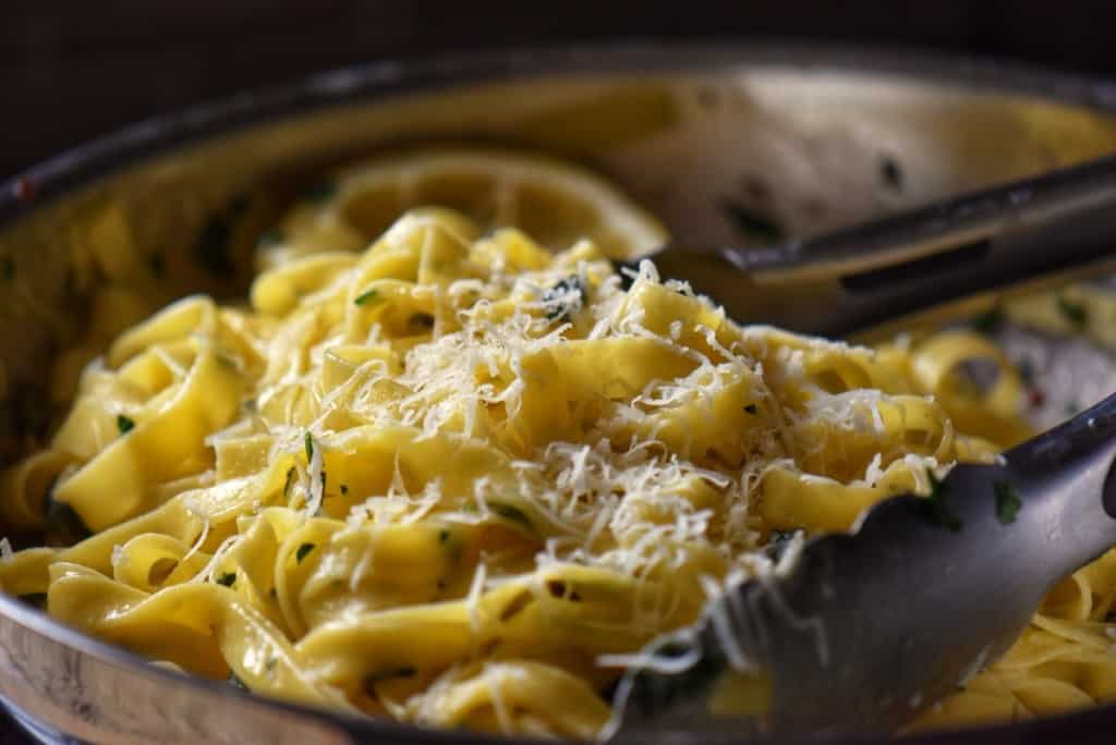 Lemon pasta tossed with grated cheese in a pan.