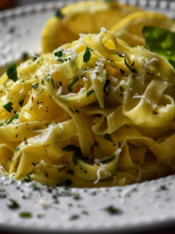 A white dish of fettuccine, garnished with chopped parsley.