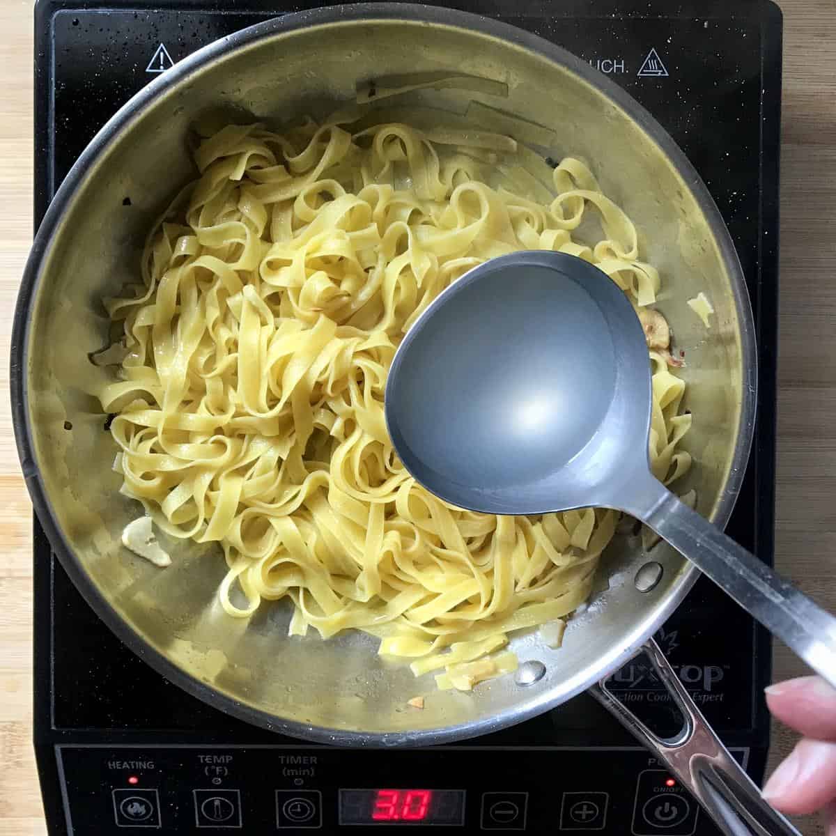 A ladle of pasta water being added to a pan of pasta.