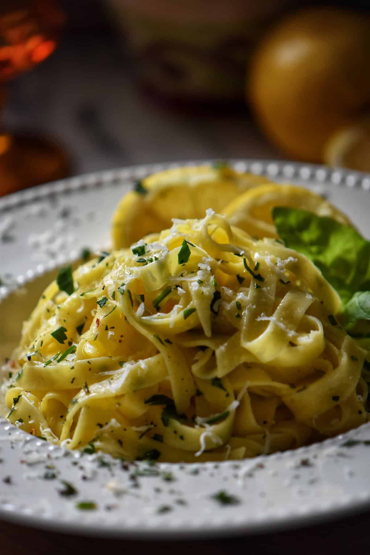 Lemon pasta in a white dish garnished with cheese and parsley.