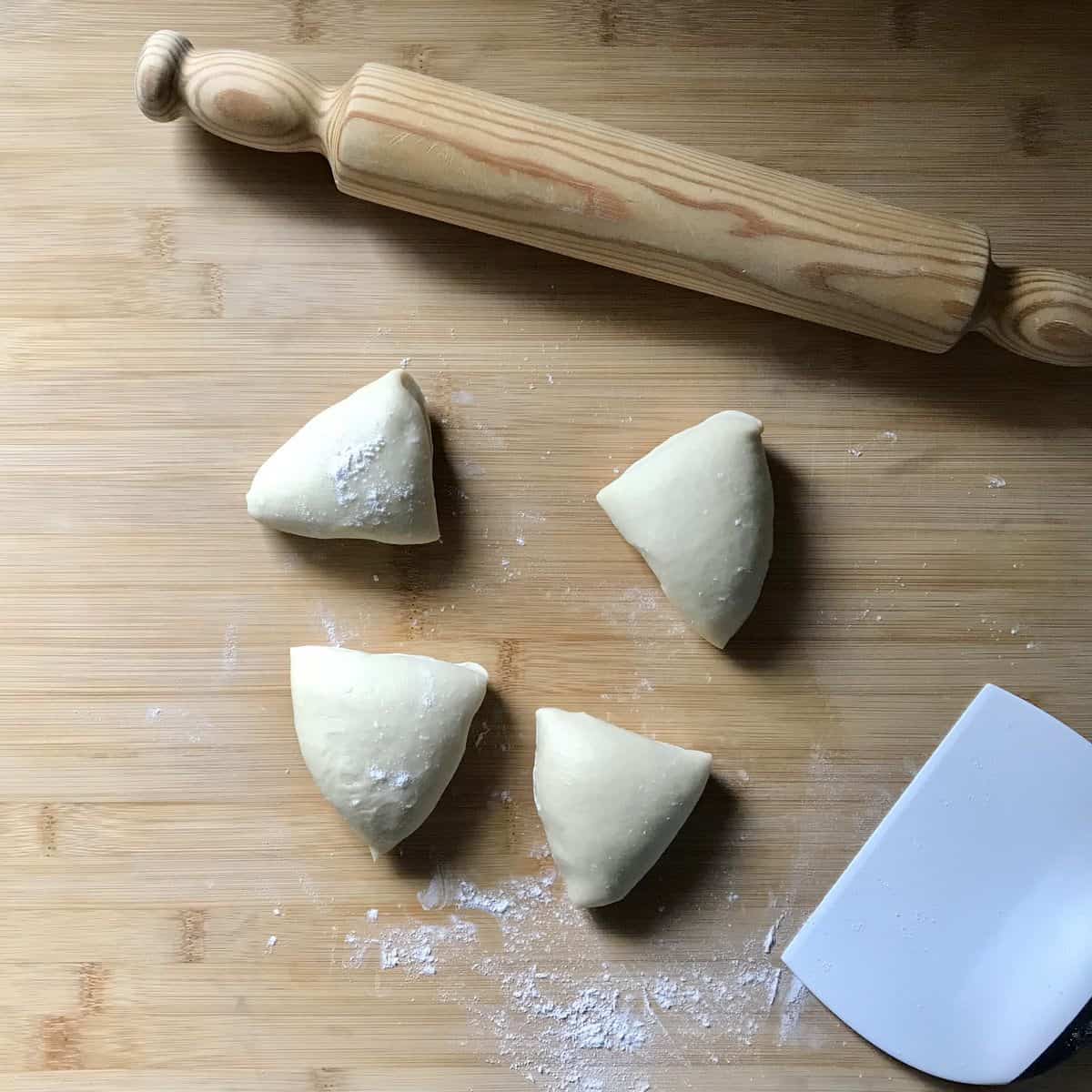 A ball of dough separated into 4 pieces next to a rolling pin.