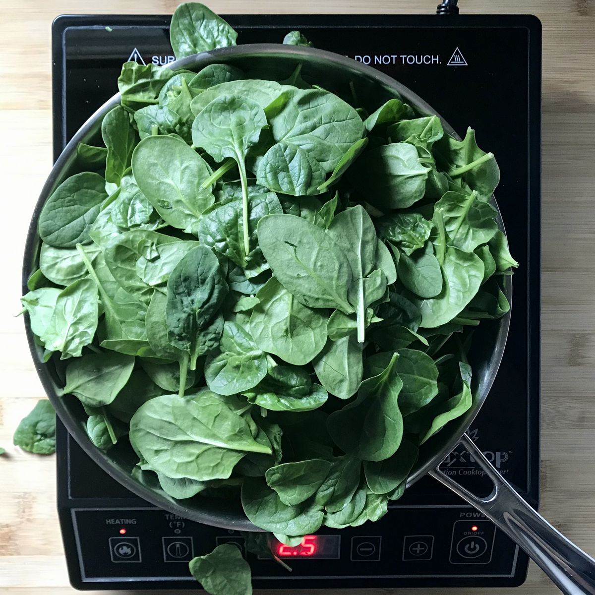 Fresh spinach added to a large skillet.