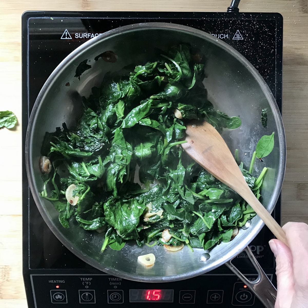 Cooked spinach with sliced garlic in a skillet.