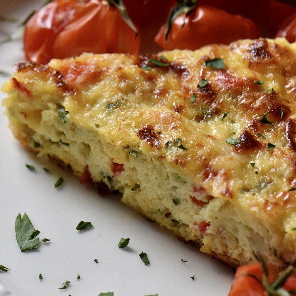 A slice of Italian zucchini frittata in a white dinner plate garnished with chopped parsley.