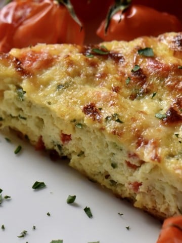 A slice of Italian zucchini frittata in a white dinner plate garnished with chopped parsley.