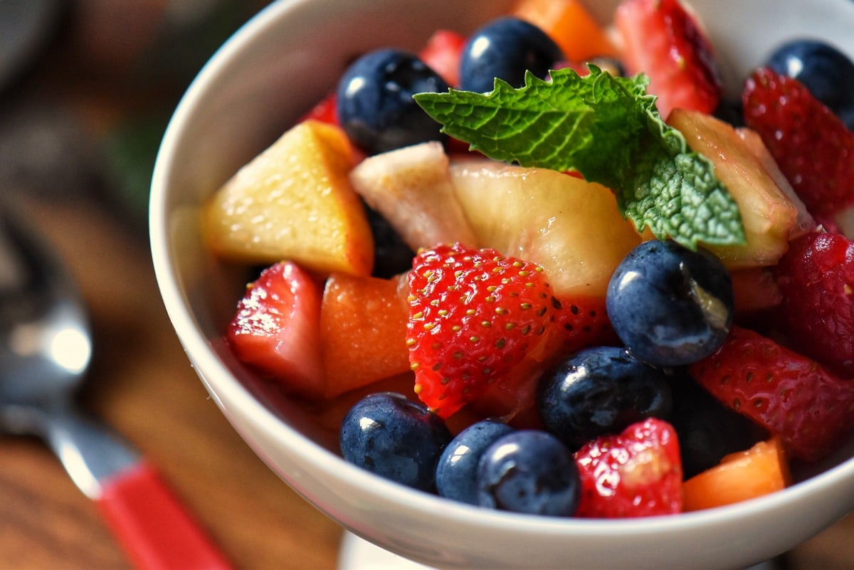 An overhead photo of cut up strawberries, apricots, pears and whole blueberries in a white serving dish.