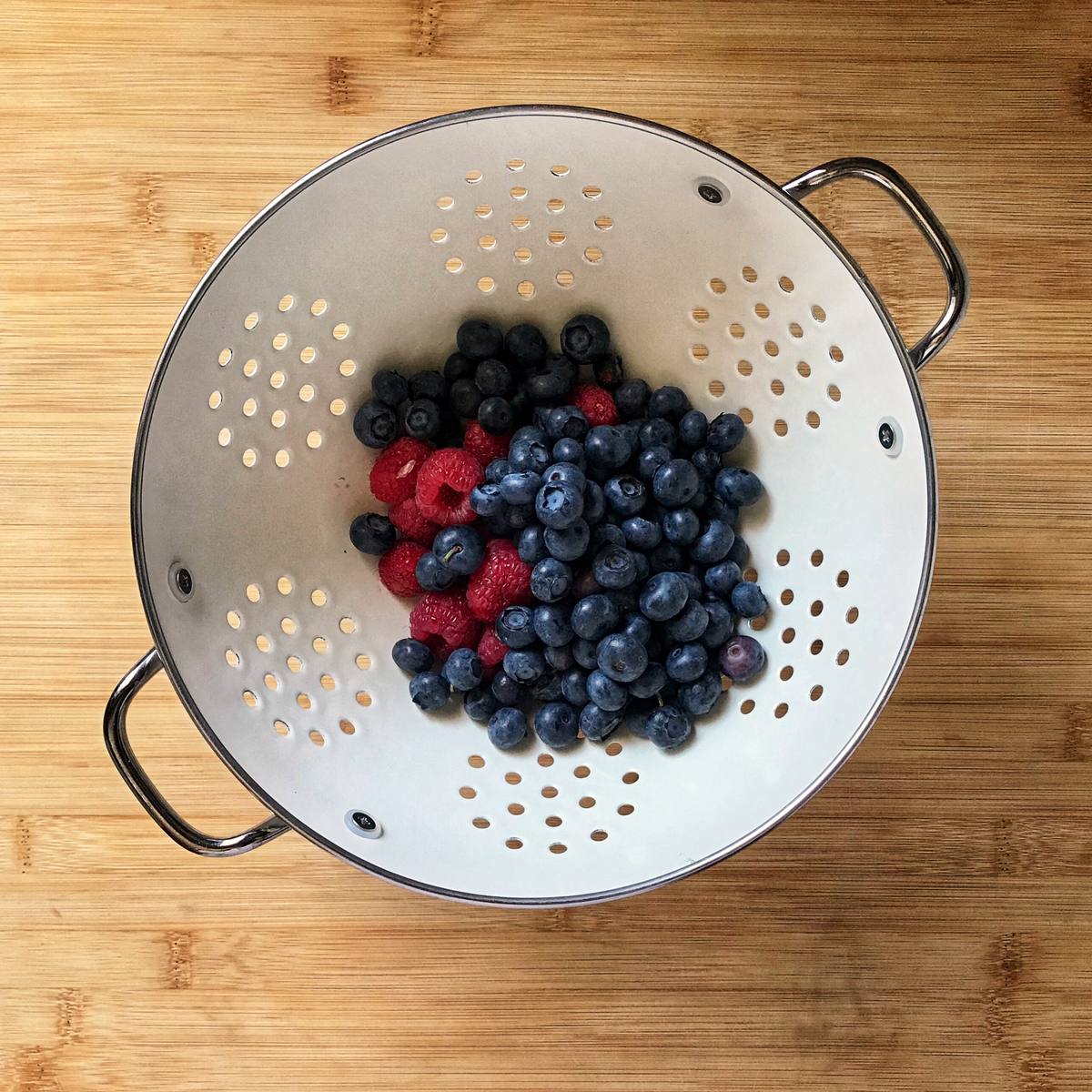 Fresh blueberries ans raspberries in a white colander. 