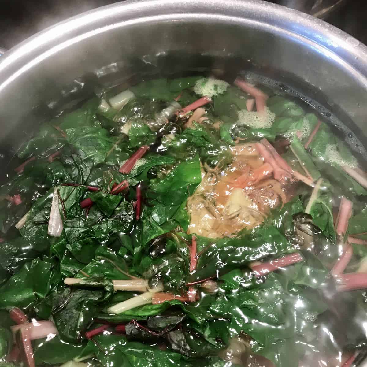 Swiss chard and potatoes simmering in a pot of water.