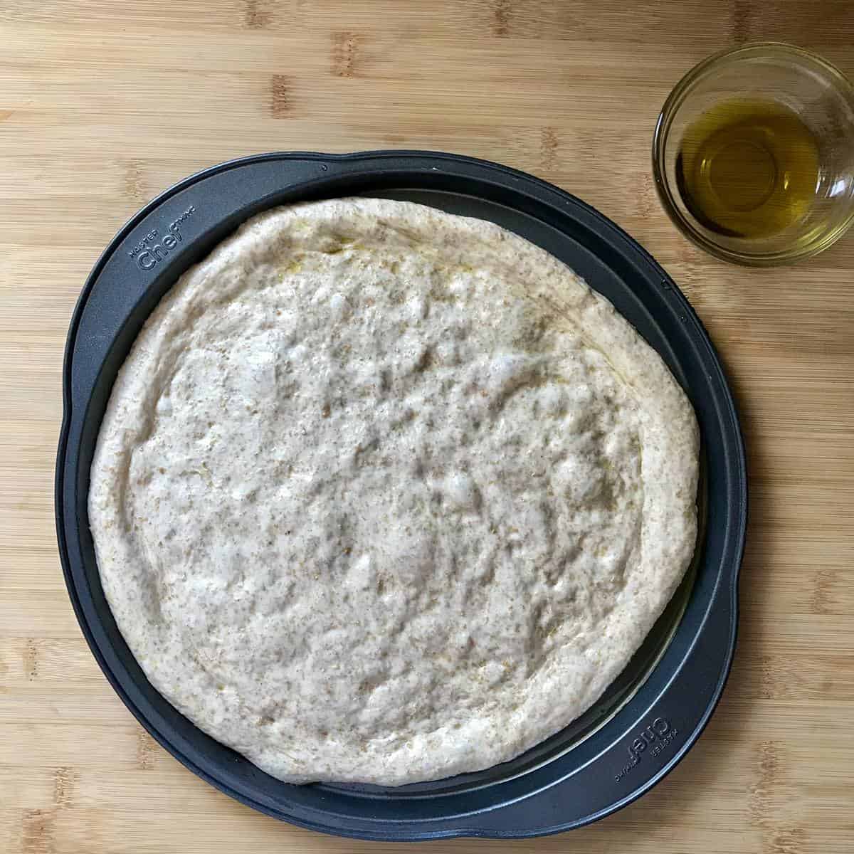 Stretched out pizza dough in a round pizza pan.