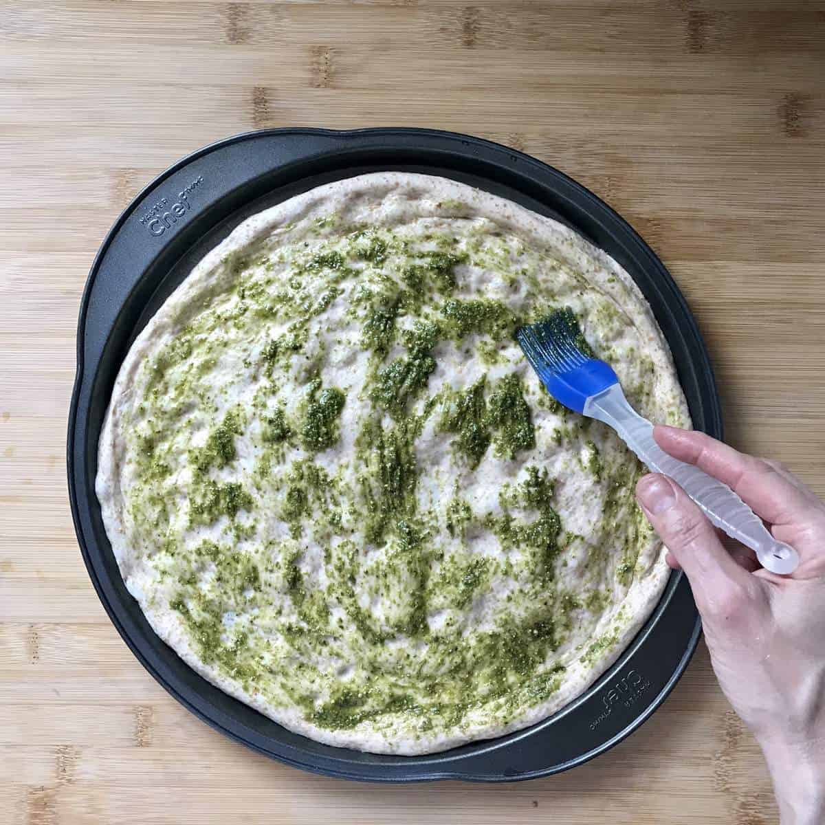 Pesto brushed on the surface of pizza dough. 