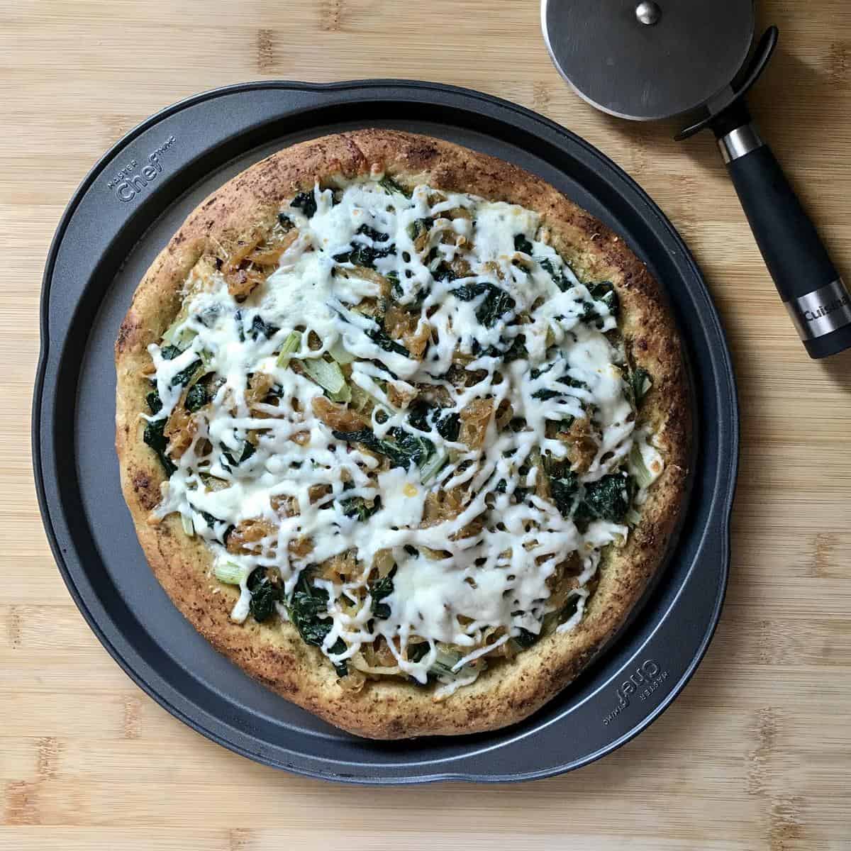 A cooked pizza on a pan next to a pizza wheel. 