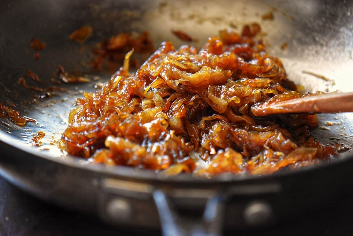 A wooden spoon stirring caramelized onions in a skillet.