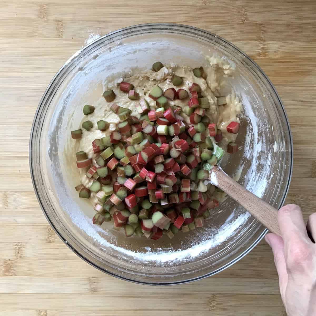 Chopped rhubarb being combined with cake batter in a bowl. 