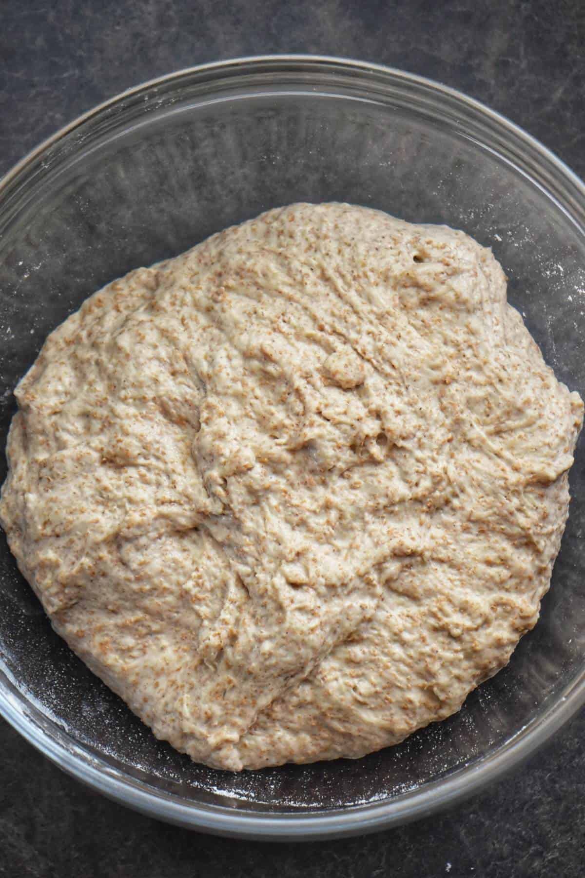 A ball of whole wheat pizza dough in a bowl.