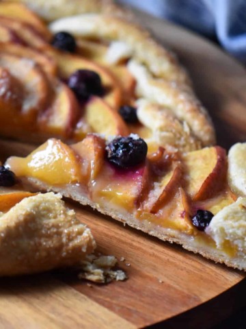 A rustic Italian tart with peaches on a wooden board.