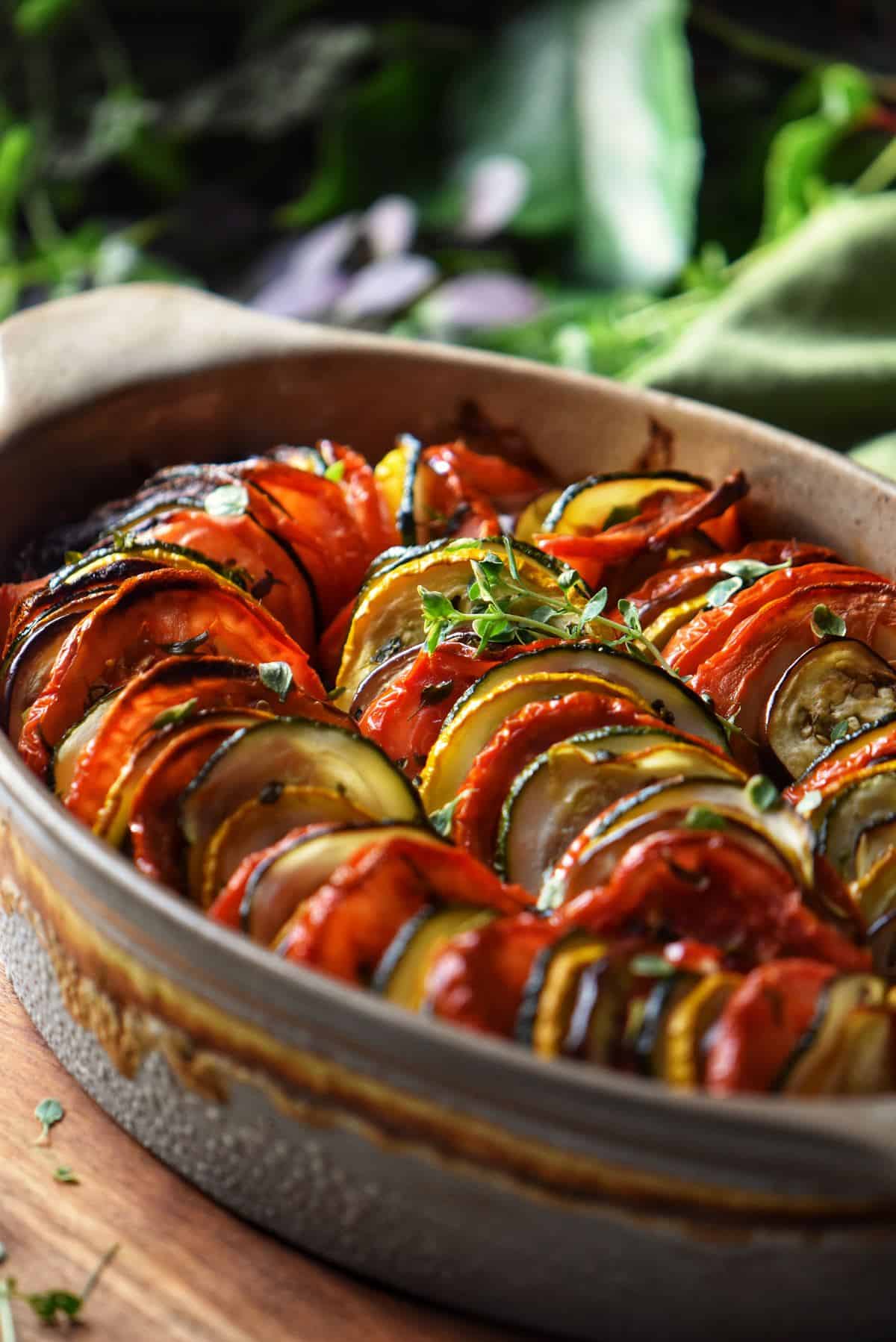 An overhead shot of Mediterranean Roasted Vegetables includes roasted peppers, eggplant, zucchini and tomatoes in a white baking dish.