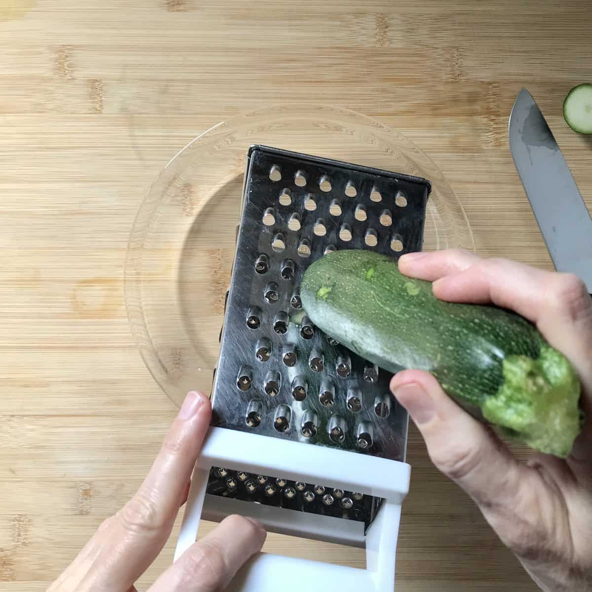 Zucchini being grated with a box grater.