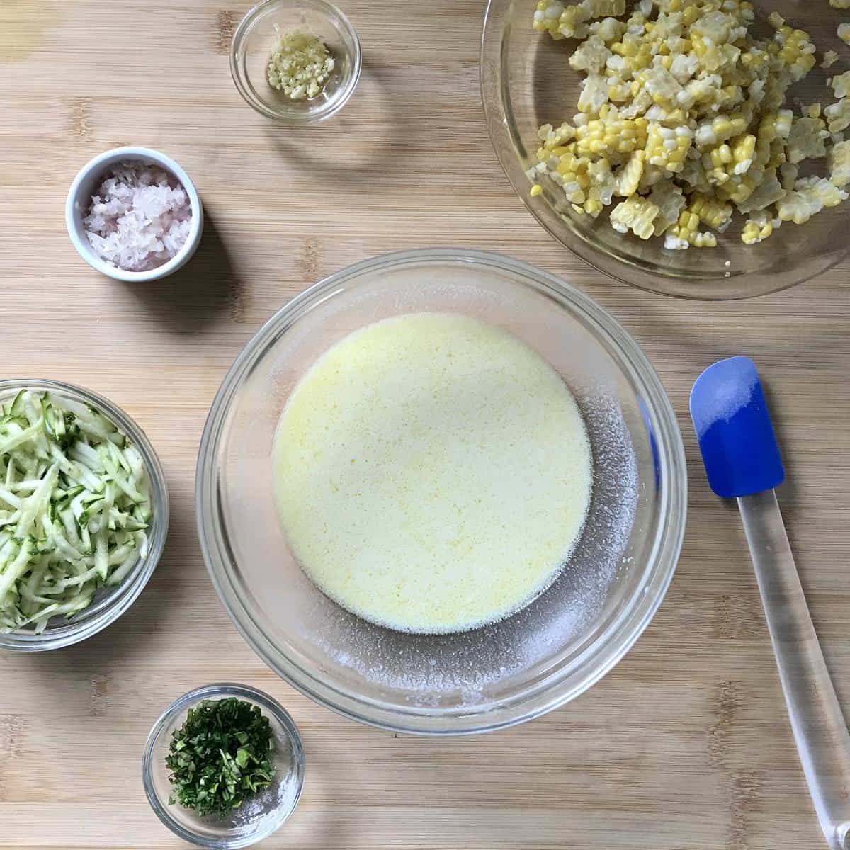 The wet ingredients to make zucchini corn pancakes on a wooden board.