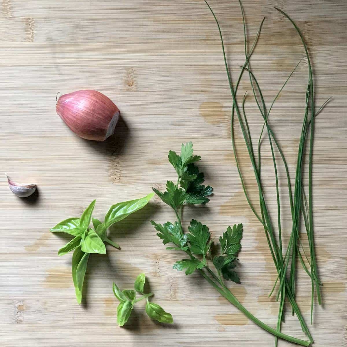 Fresh herbs, garlic and a French shallot on a cutting board.