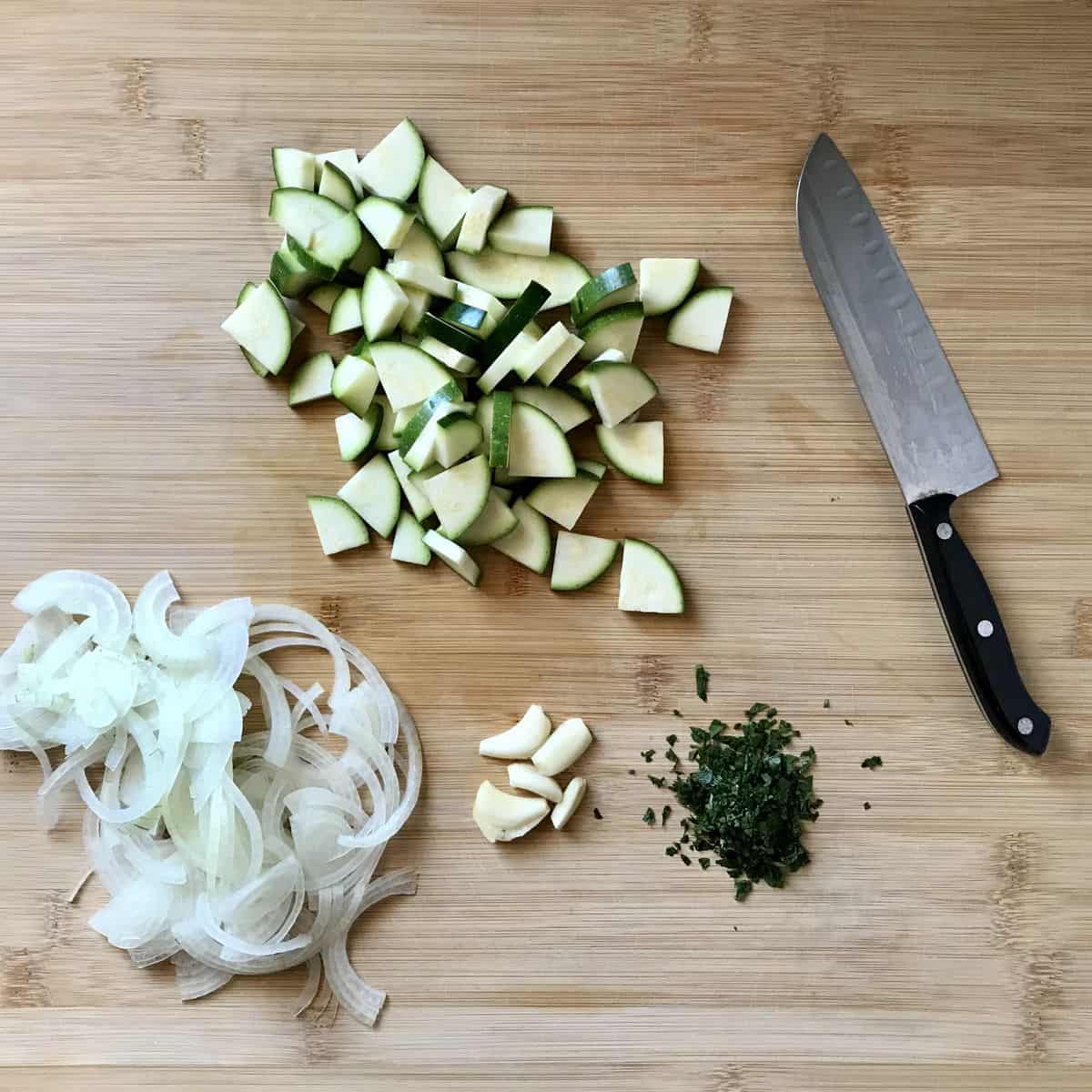 Sliced onions, quartered zucchini, minced parsley and sliced garlic on a wooden board.