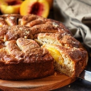 A slice of fresh peach cake being removed from the whole cake.