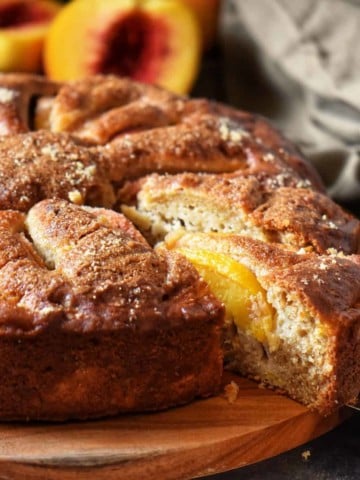 A slice of fresh peach cake being removed from the whole cake.
