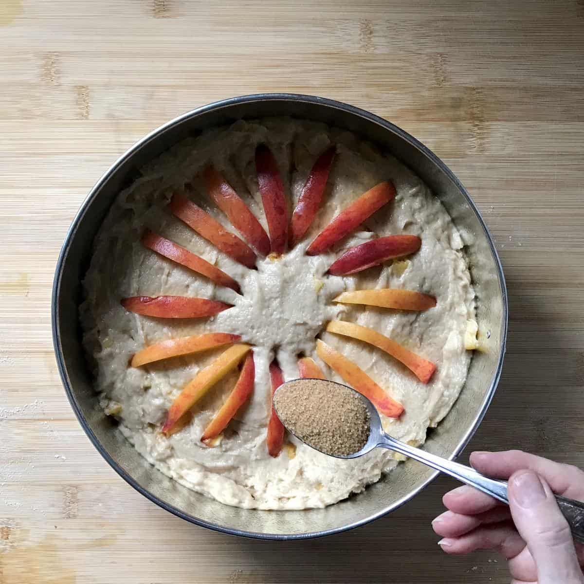 Turbinado sugar being sprinkled on a peach cake.