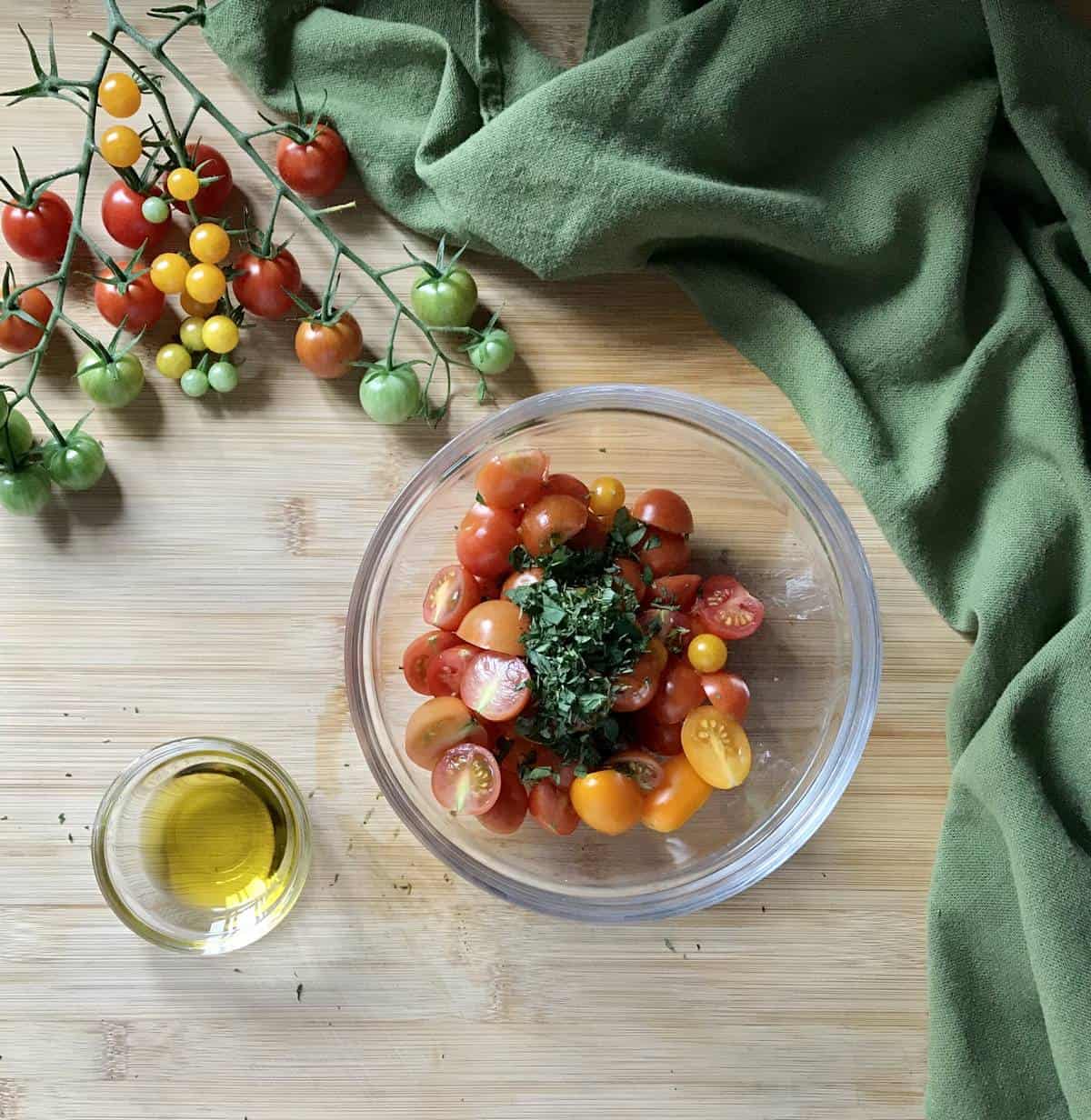 Sliced cherry tomatoes and herbs in a mixing bowl. 
