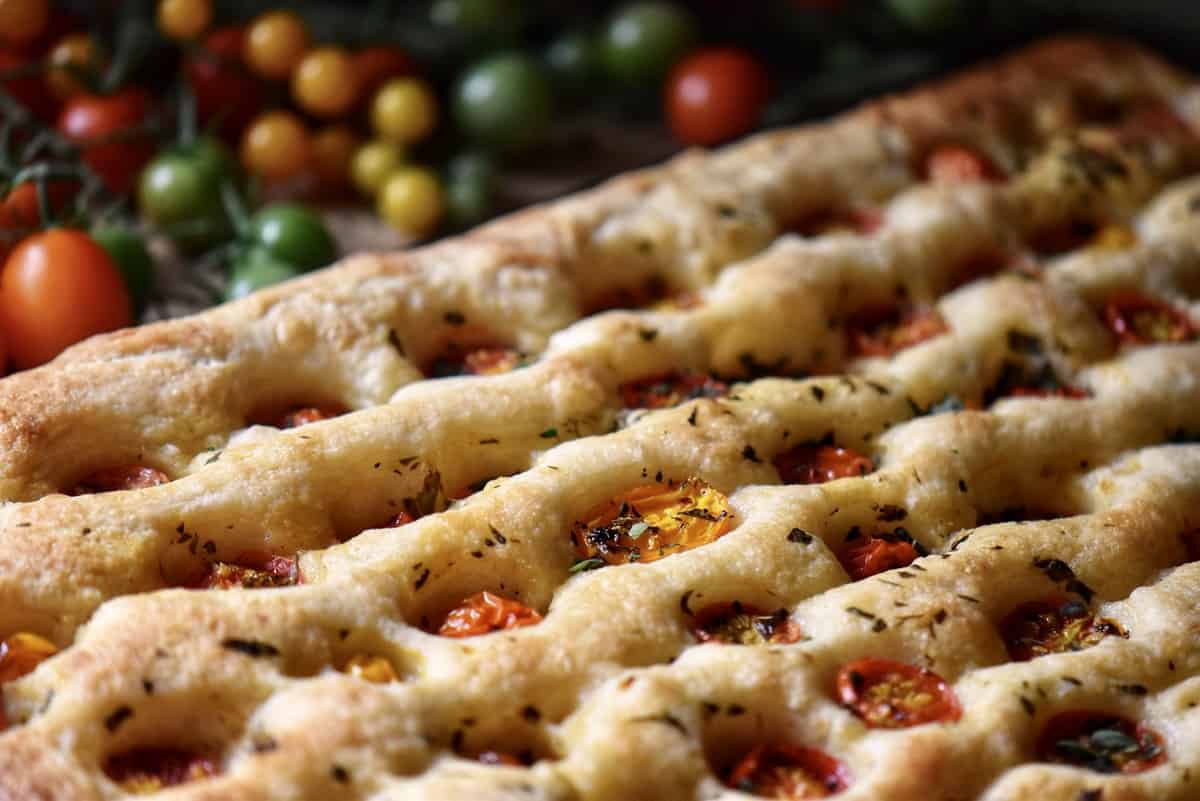 A side view of focaccia bread with cherry tomatoes in the background. 