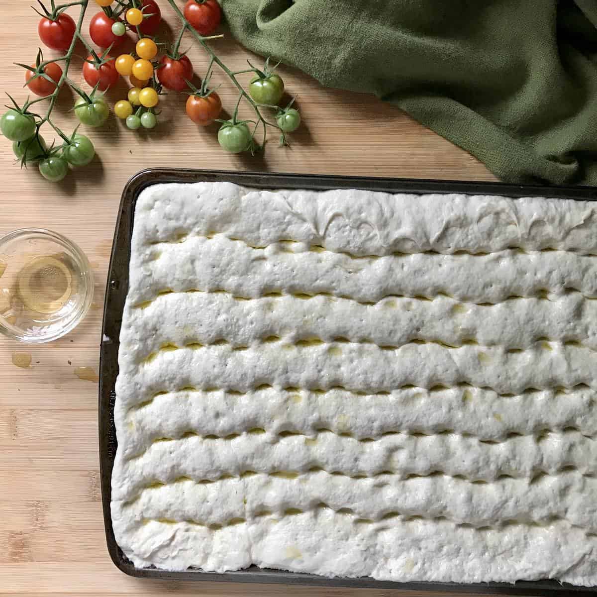 Dimpled focaccia bread in a sheet pan before baking. 