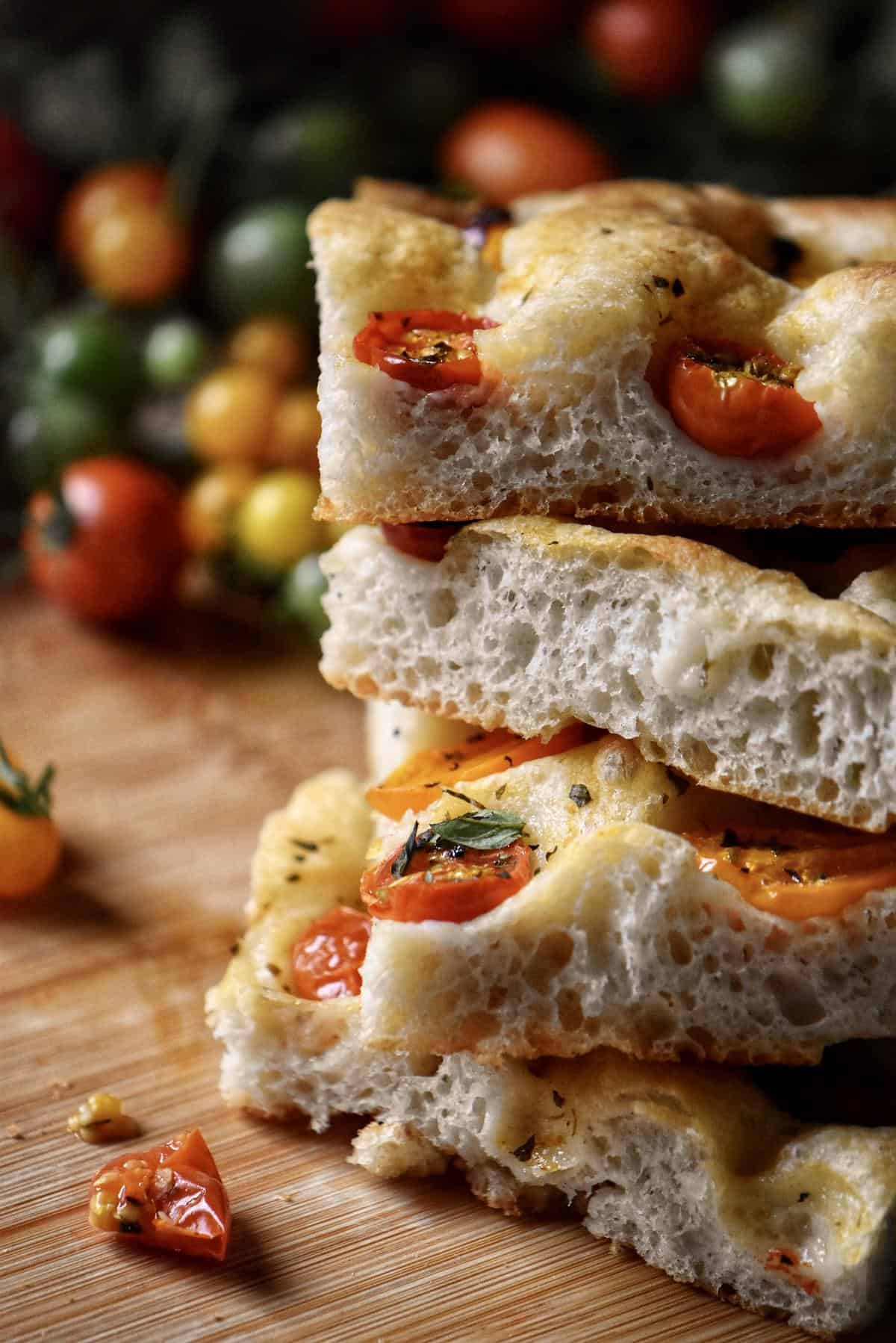 A stack of sliced cherry tomato focaccia bread on a wooden board. 