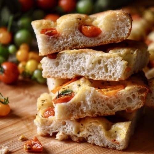 A stack of sliced cherry tomato focaccia bread on a wooden board.