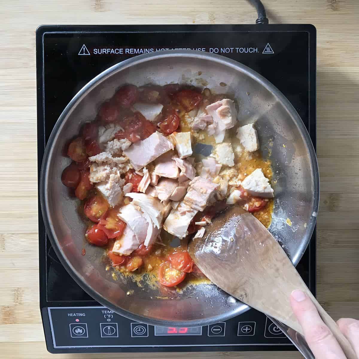 A can of tuna added to a pan of sauteed cherry tomatoes.