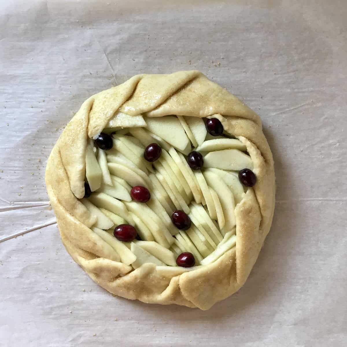 An overhead photo of an apple crostata topped with cranberries.